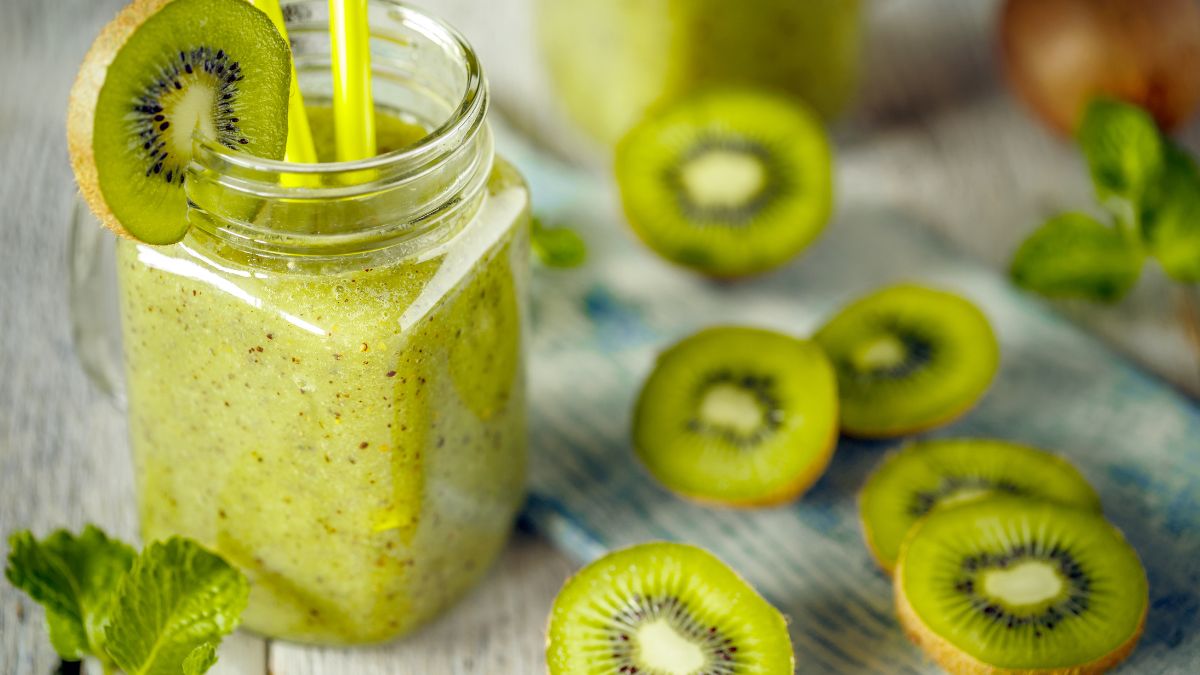 Friss kivi turmix egy üvegben, kivi szeletekkel és mentalevelekkel díszítve.