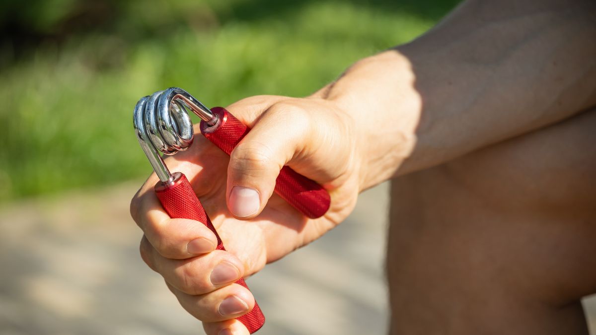 Egy kéz marokerősítő eszközt tart, amely segít az ujjak és csukló erősítésében.