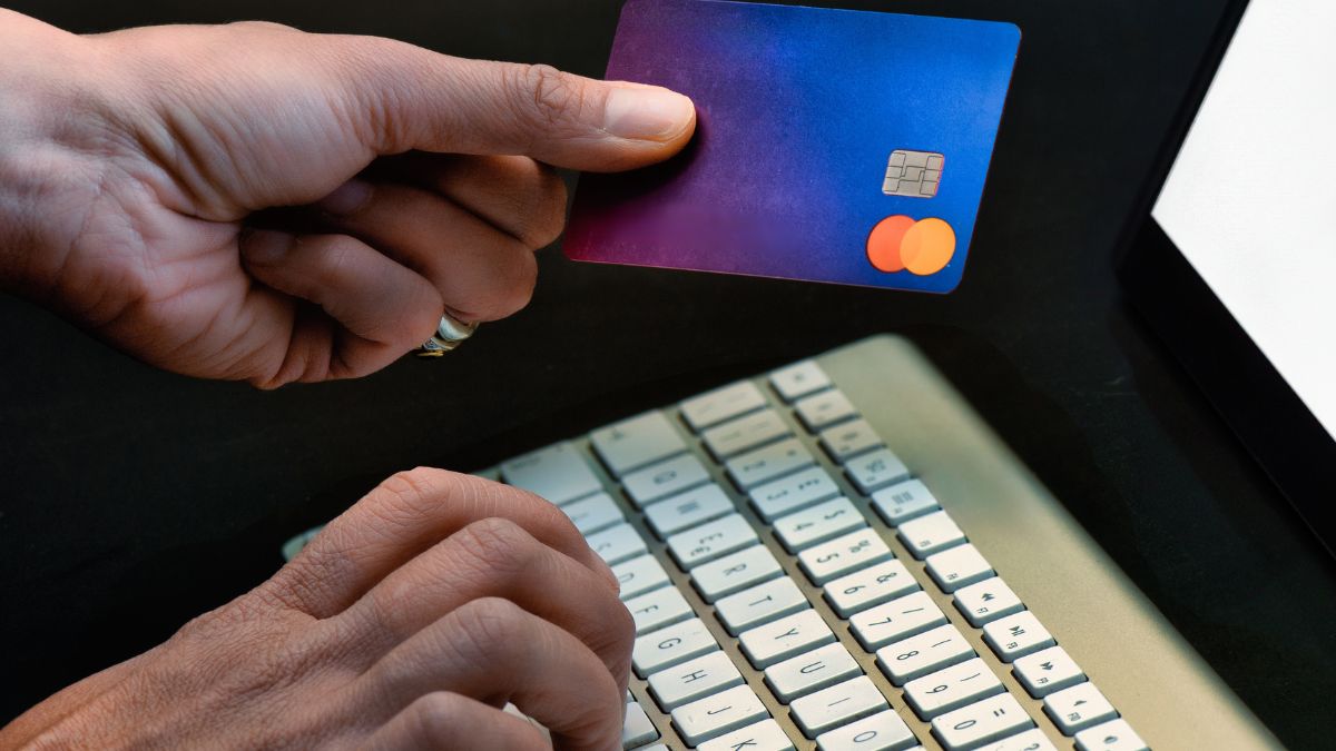 Egy kéz egy bankkártyát tart, miközben a másik kéz a billentyűzeten gépel.