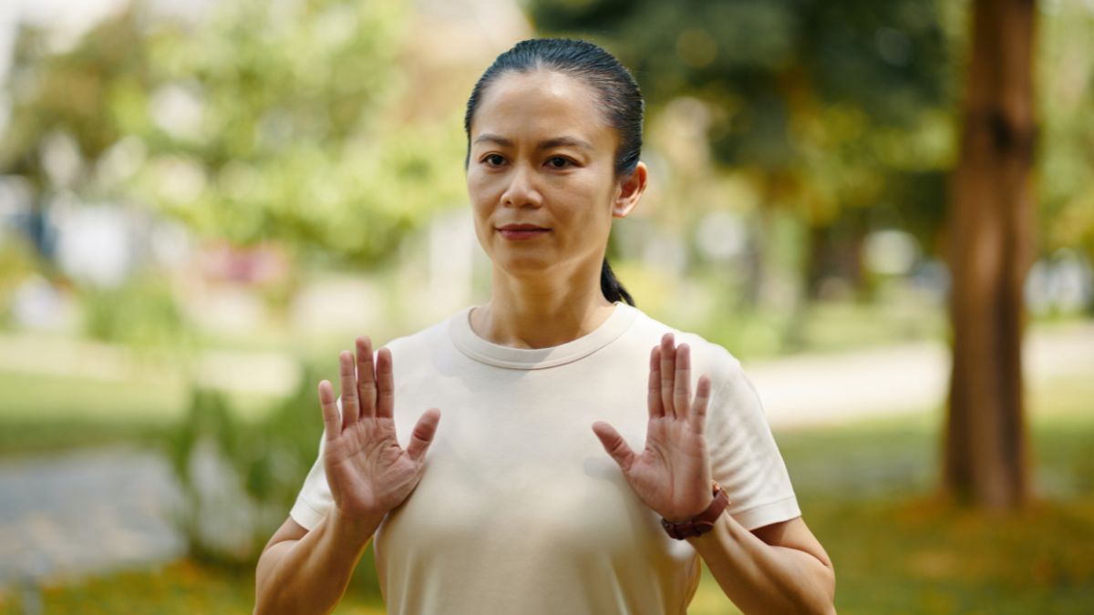 Egy nő tai chi-t gyakorol a szabadban, nyugodt arckifejezéssel.