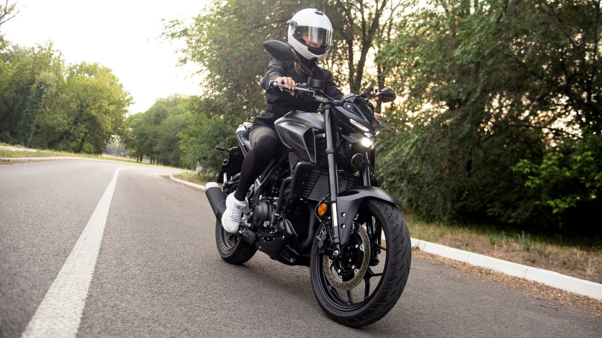 Egy motoros nő fekete motoron ül, védőfelszerelésben, egy csendes úton.