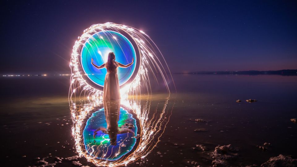 Egy nő áll a vízben, kezében fénykörrel, amely álomszerű hatást kelt.