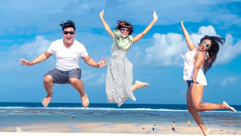 Három fiatal felnőtt ugrik a tengerparton, boldog és felszabadult pillanatban.