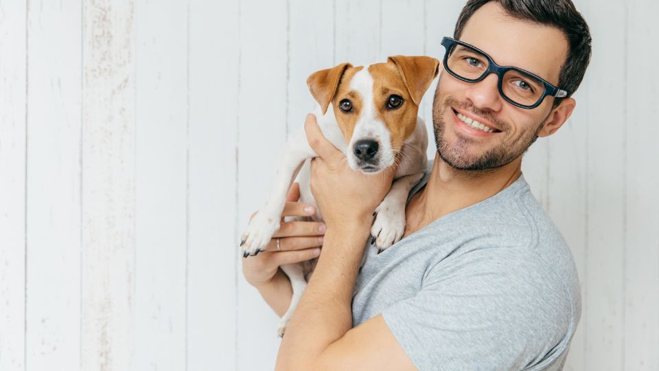 Egy férfi ölel egy kutyát, mosolyogva néz a kamerába.